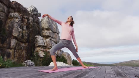 caucasian woman practicing yoga outdoors, stretching standing on deck in rural mountainside setting