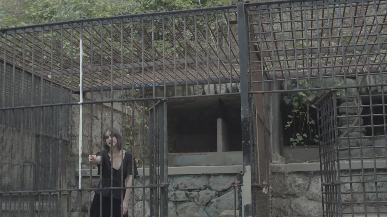 Wide shot of a gothic woman inside of a rusted cage closes the big steel door