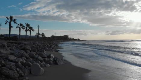 early-morning-coastline-as-the-waves-gently-wash-up-on-shore,-captured-from-a-low-drone-shot-that-gracefully-flies-over-the-stunning-seascape