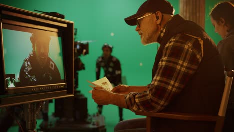 director looks at display and compares to storyboard while shooting blockbuster movie. green screen scene with actor wearing motion caption suit. studio set professional crew doing high budget movie