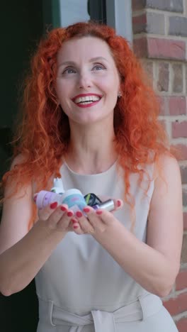 a cheerful woman holding a variety of beauty products in her hands radiating joy a joyful woman with red hair embraces her beauty collection outdoors showcasing her happiness and confidence