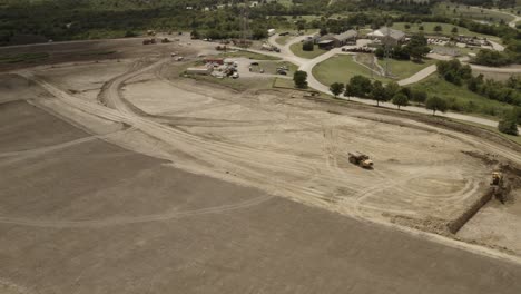 a dump truck follows the tracks made on a construction site with a front loader in the distance scooping up dirt