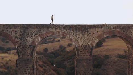 ariel fotografió a un hombre elegante y cariñoso caminando por un pequeño puente en italia en un caluroso día de verano por la tarde.