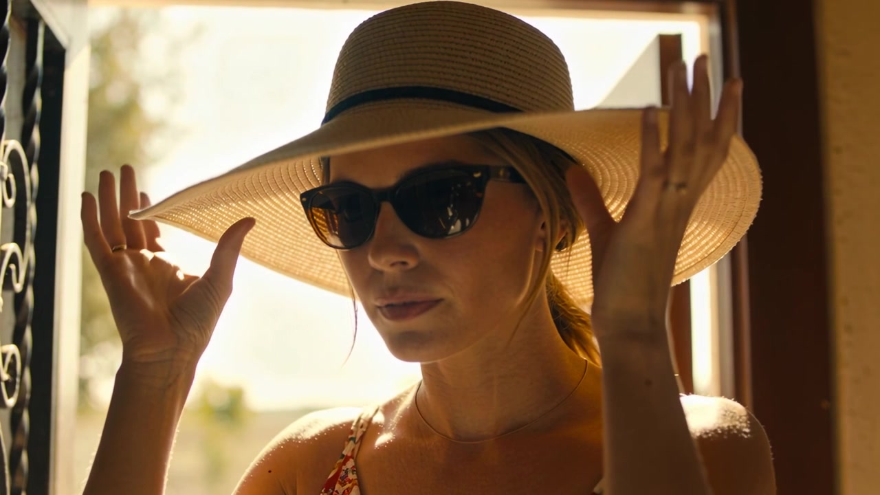 Raising dark sunglasses, woman in straw sun hat adjusting at home doorway as sunlight urging exit