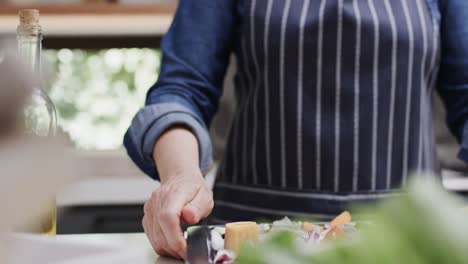 midsection of senior caucasian woman holding baking tray with vegetables in kitchen, slow motion