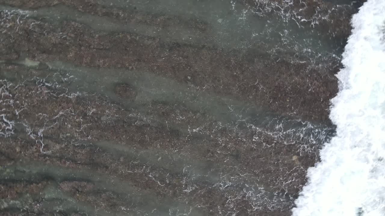 Aerial Top-Down View of Ocean Waves Crashing Over Rocky Seabed