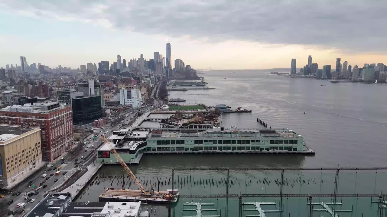 Horizontal drone pull-away shot over 11th Avenue in New York along the Hudson River, revealing the city's waterfront, towering skyscrapers, and stunning Manhattan skyline with smooth aerial motion.