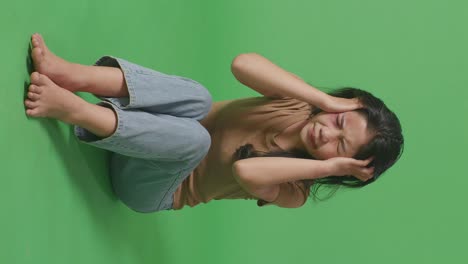 full body of young asian woman victim of violence with bruise on body stressing and having a headache while sitting in the green screen background studio