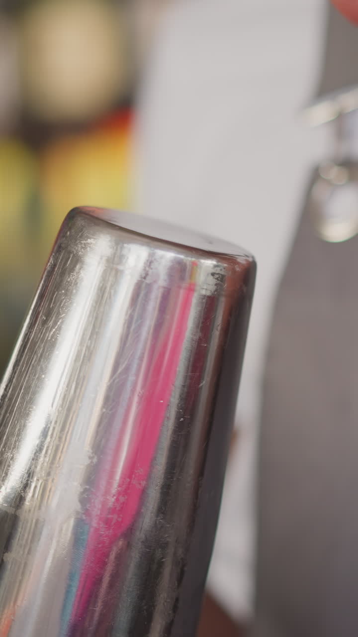 el barman negro toca el fondo del sacudidor brillante en el bar de primer plano. el barman afroamericano sacude las gotas de cóctel de la taza en el club nocturno. el hombre prepara la bebida