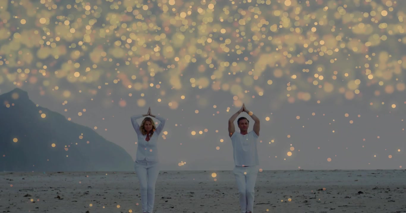 Man and woman walking on beach, golden particles drifting revealing pair lifting palms for yoga