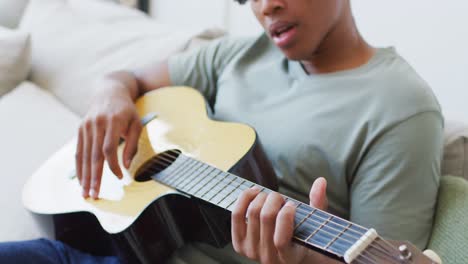 feliz hombre afroamericano toca la guitarra y canta en casa
