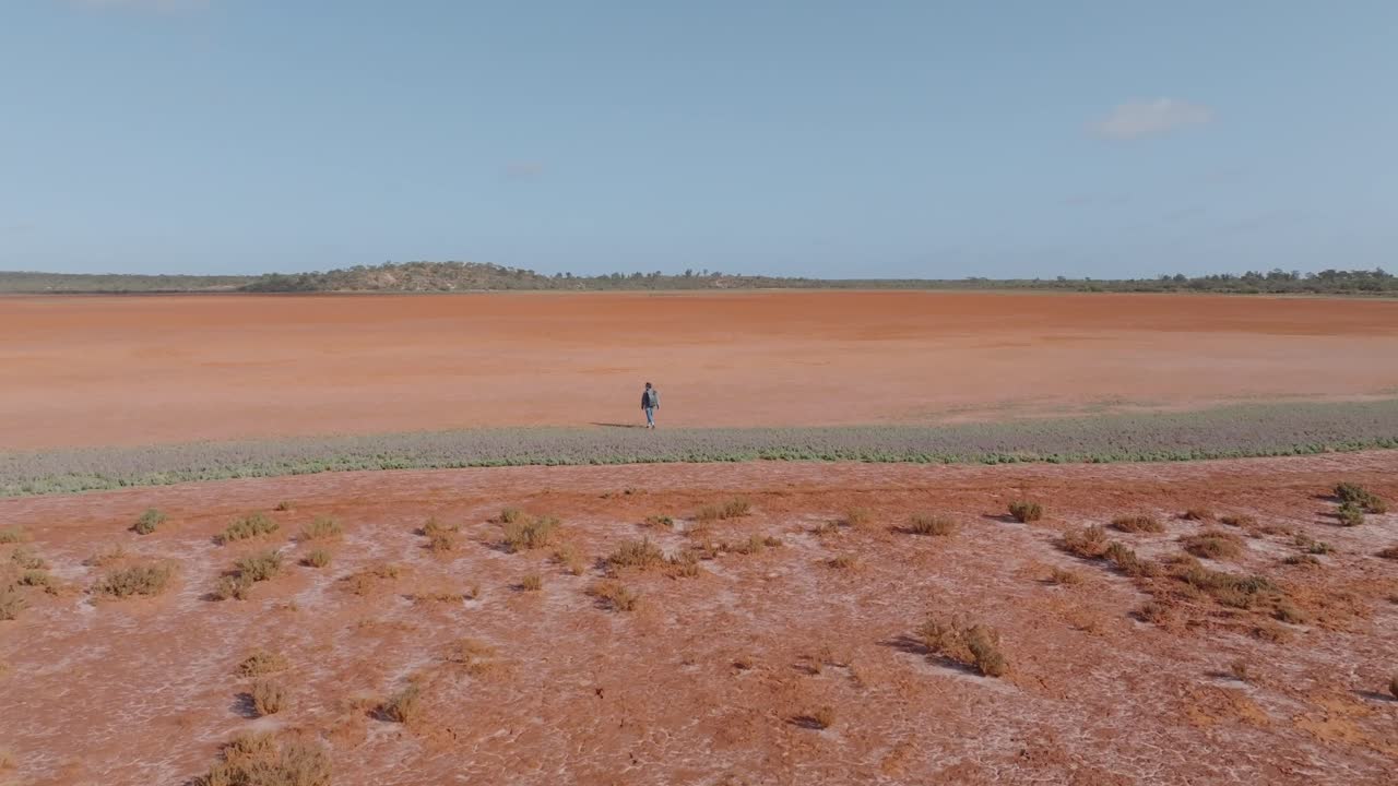 Solitary figure walking across a vast red dry lake