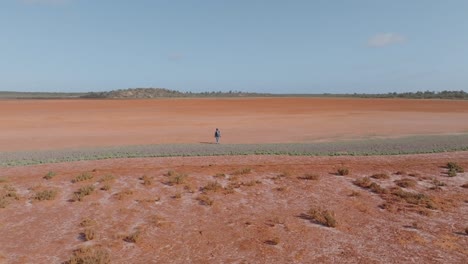 solitary figure walking across a vast red dry lake