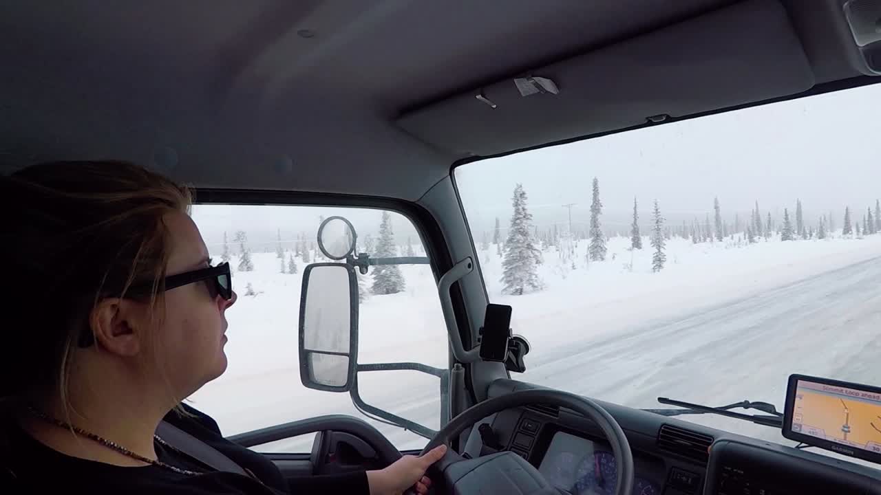 Woman driving on a snowy road, surrounded by arctic Sitka forest, GPS on, at snowfall, in Alaska, USA