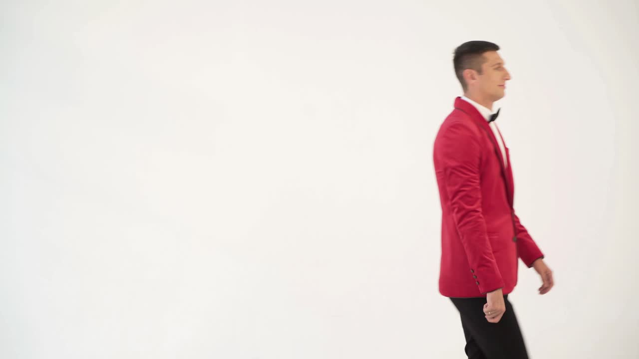 showman in a red jacket with a bow tie is circling around himself with openarmed hands in different sides on a white background
