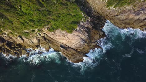 Aerial-top-down-view-of-sea-waves-hitting-on-the-low-cliffs-near-Bombinhas