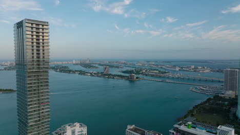 Fly-above-tall-buildings-on-waterfront-at-twilight.-Aerial-view-of-bridges-and-islands-in-bay.-Miami,-USA