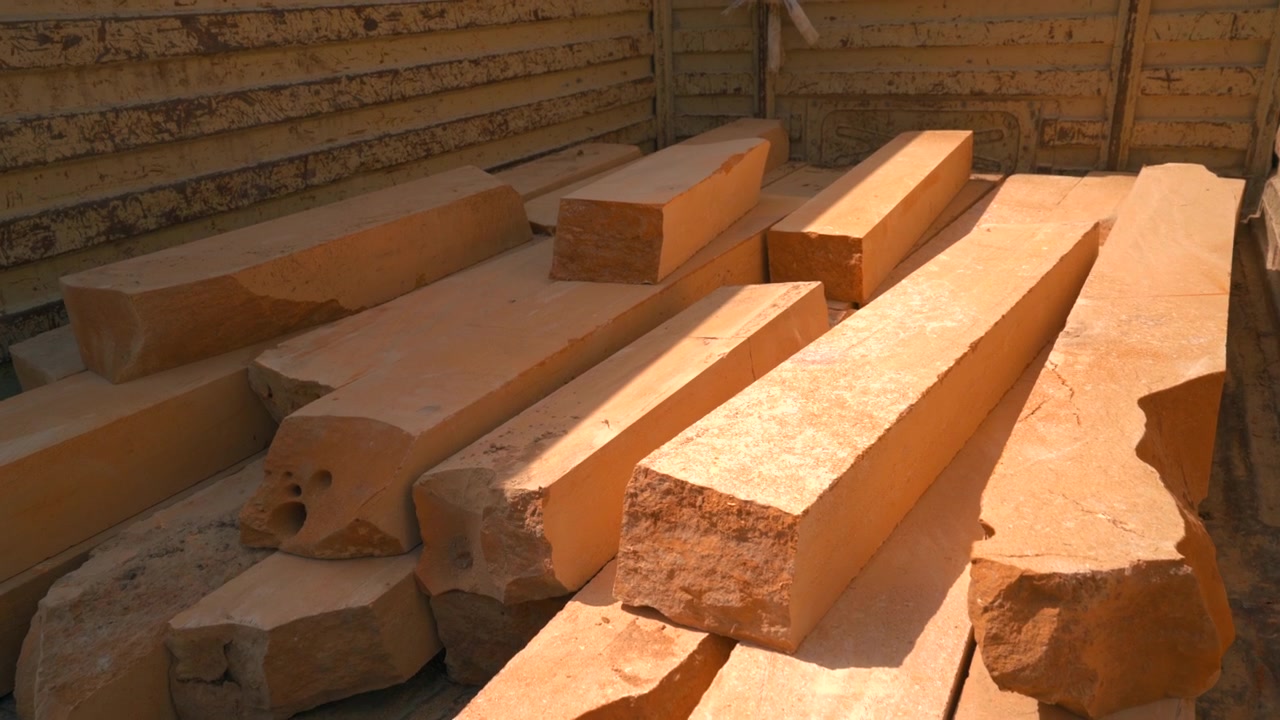Cinematic static shot of raw golden sandstone blocks and beams loaded on a transport bed in Jaisalmer, Rajasthan, India.