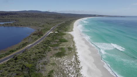 gardens road along white sandy beach and sloop lagoon in binalong bay, tasmania