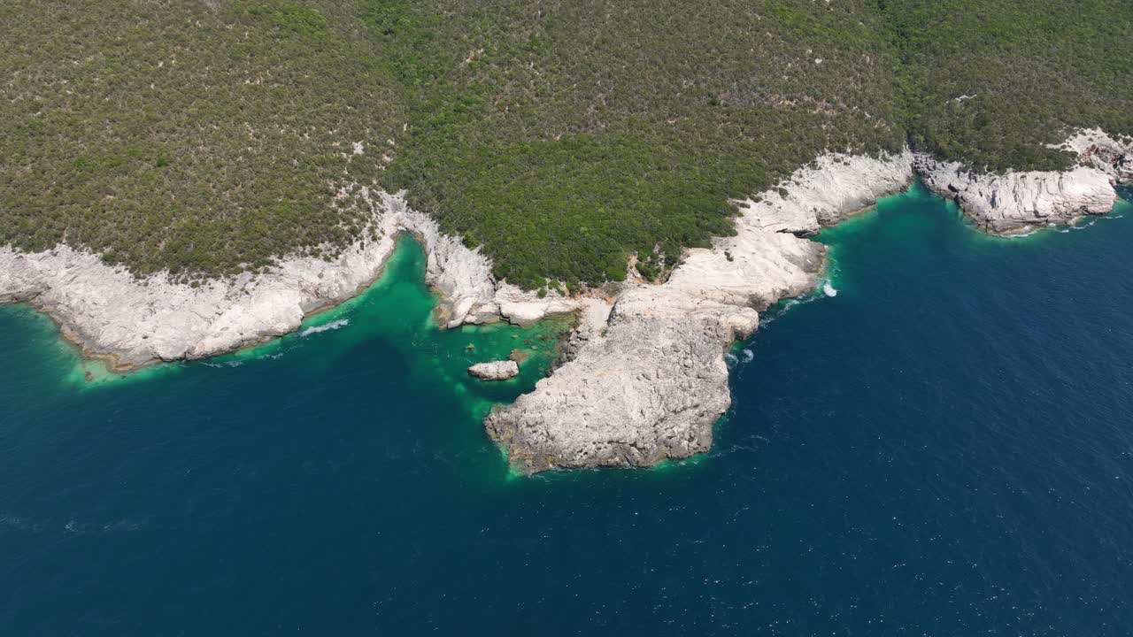 A stunning high-angle drone shot of the rugged, rocky coastline of Dugi Otok, Croatia. The clear Adriatic Sea is a vibrant turquoise against the white cliffs