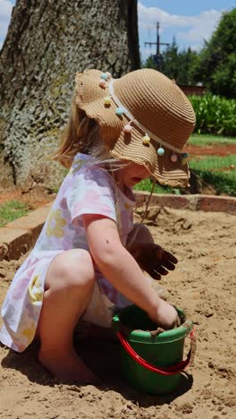 vertical shot of little blonde girl playing with mud in sandbox at playground making mud pies. outdoor creative activities.