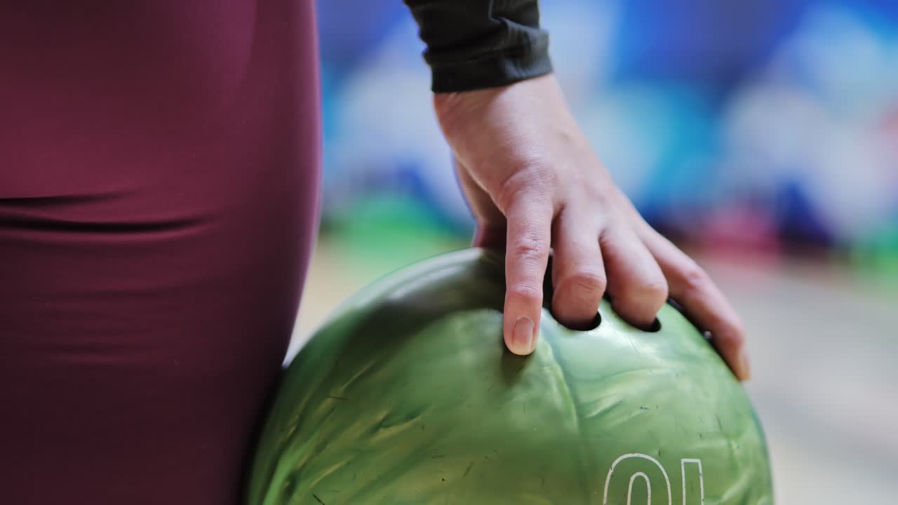 Close-up shot of woman preparing bowling throw with fingers set in green ball holes
