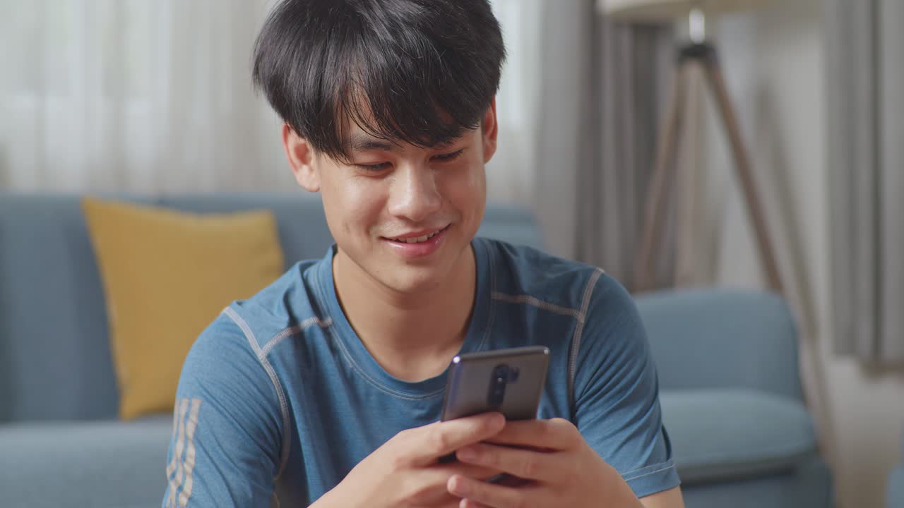 행복하고 운동적인 건강한 아시아 남자가 스포츠 옷을 입고 집에서 아침 운동을 한 후 휴대전화를 사용하고 있습니다.