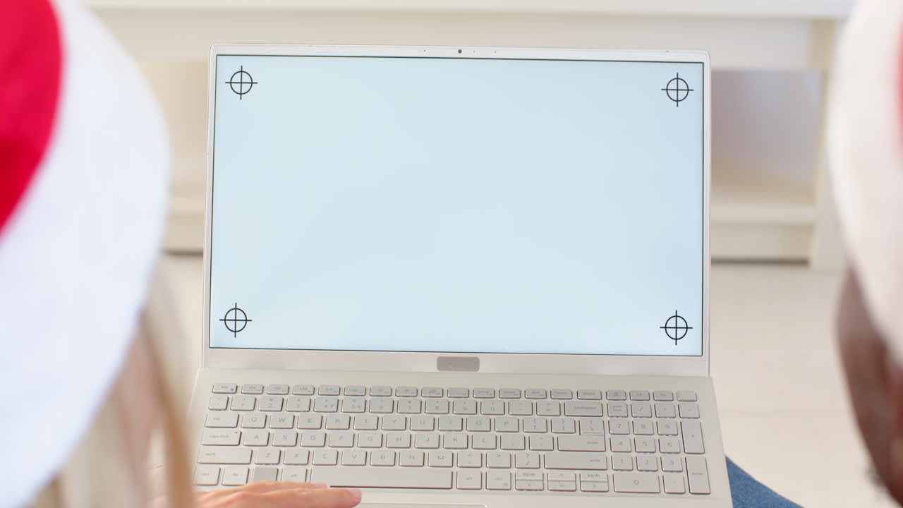 diverse couple wearing Santa hats using laptop at home during Christmas, copy space