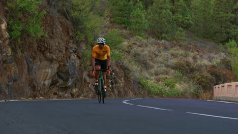 un hombre vestido con una camiseta amarilla está en bicicleta en una carretera situada a gran altitud en las montañas utilizando una bicicleta de carretera deportiva