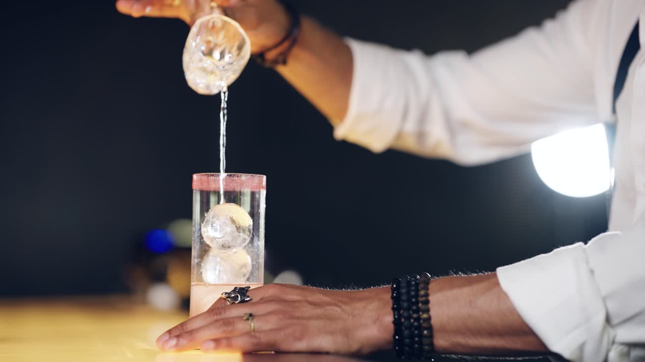 Professionele barman schenkt cocktail in glas met ijssferen