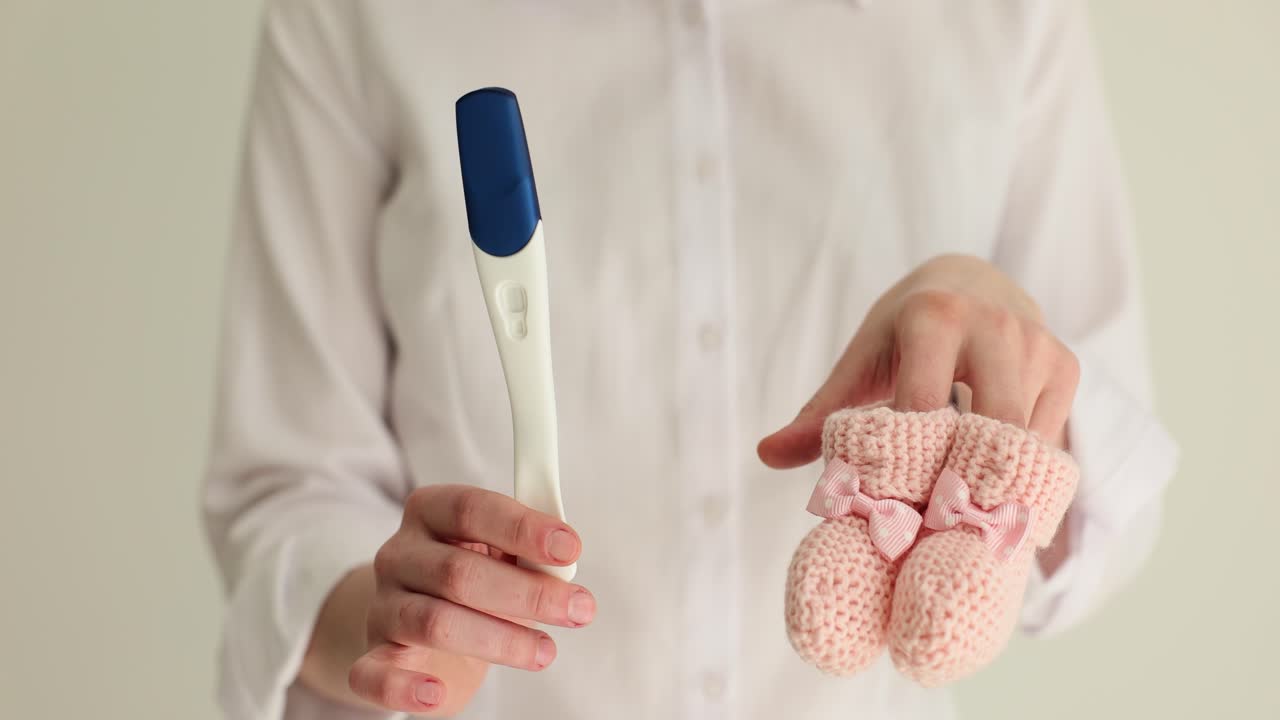 Woman holds pregnancy test and pink knitted socks in hands