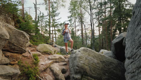 una mujer con una mochila en la espalda está de pie sobre enormes piedras en el bosque caminando y vida activa