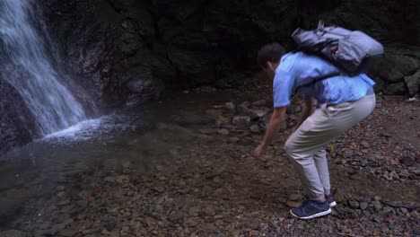 a male hiker washes his face in the pond next to a small waterfall in japan - midshot