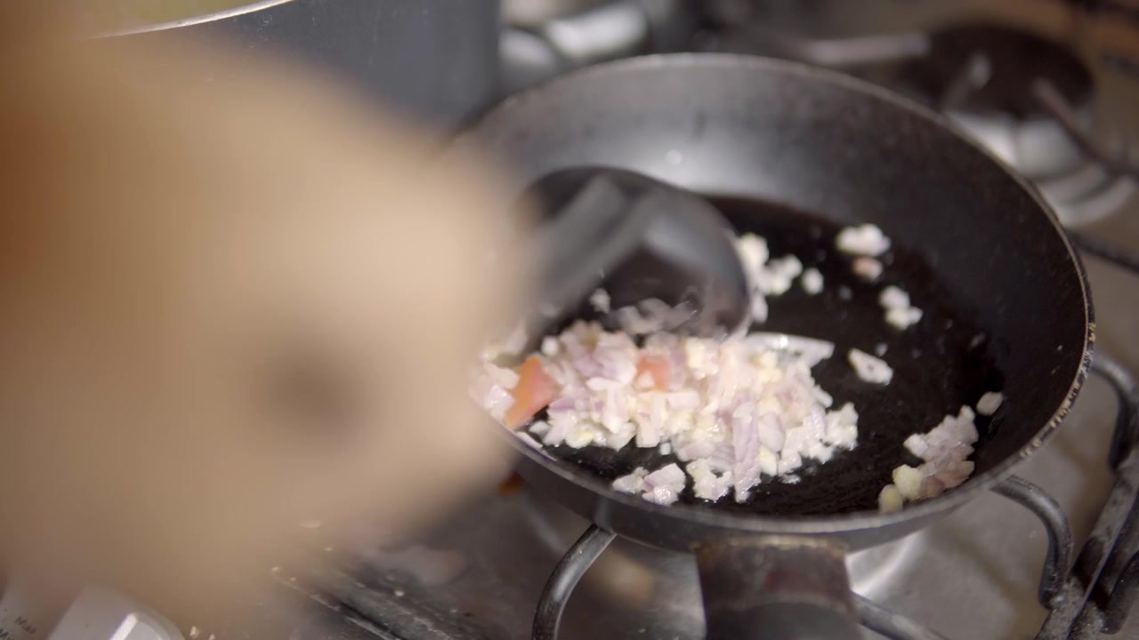 Nahaufnahme von gehackten Zwiebeln, die in einer Bratpfanne auf einem Gasherd während der Zubereitung einer hausgemachten Mahlzeit in der Küche angebraten werden