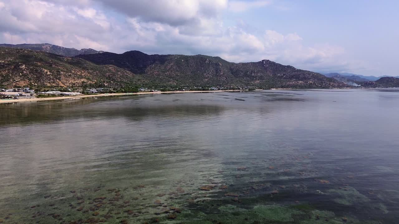 Drone circles lighthouse while ascending, revealing mirrorlike sea and distant horizon on a calm, windless day along Vietnam’s stunning coastline.