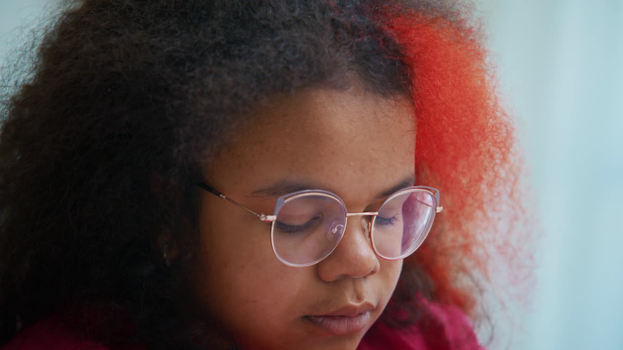 Portrait of a young African American girl with colorful curly hair adjusting and wearing her eyeglasses, looking at camera and closing her eyes