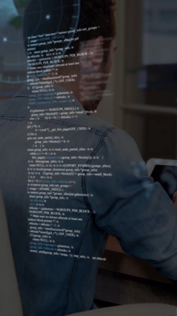 Vertical video: Man sitting at desk tapping tablet and revealing code overlays for tech analysis