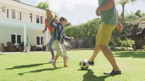 happy caucasian couple with son playing football in garden