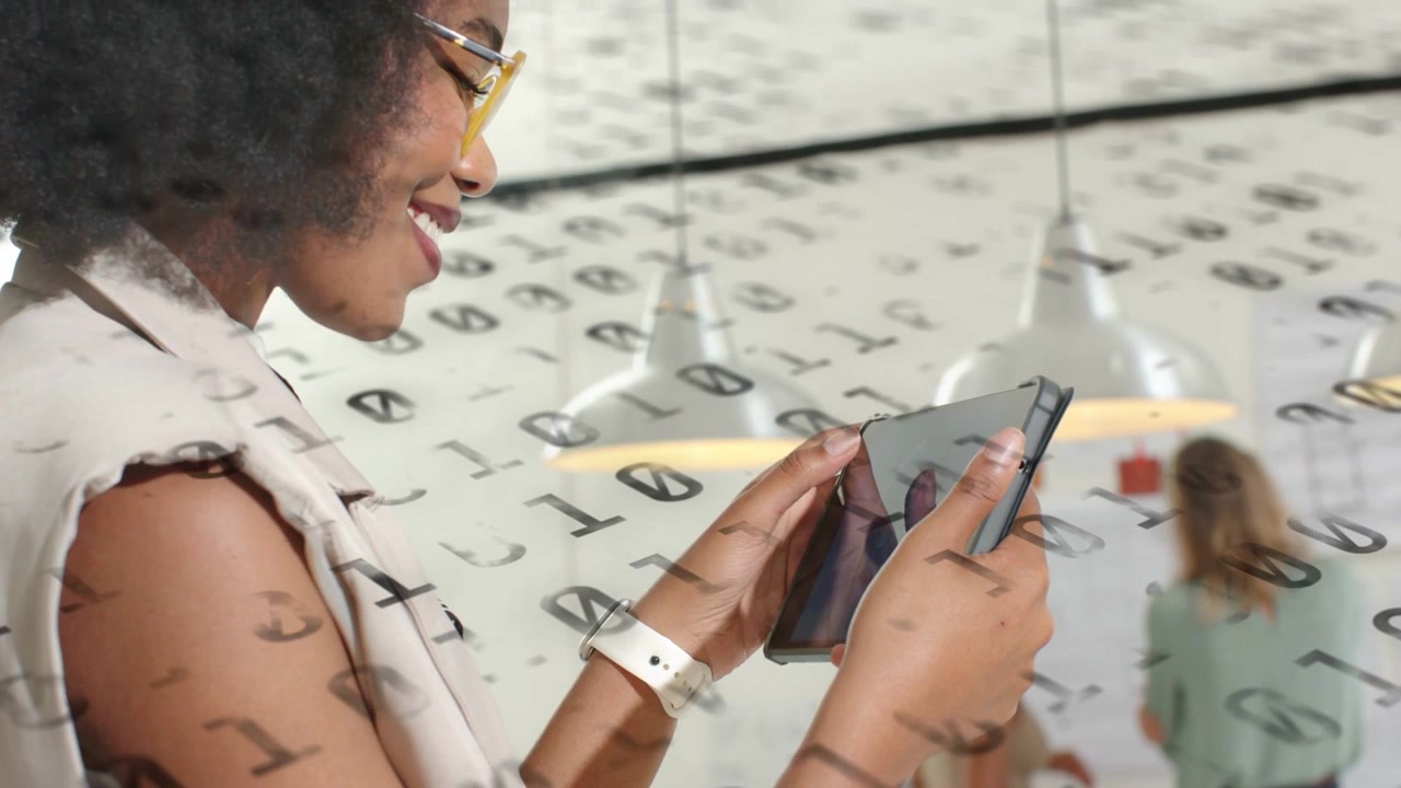 Woman tapping tablet in open office activating binary overlay and analyzing tech data while smiling
