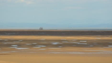 Sonnenflecken-Und-Wolkenschatten-Rasen-über-Unebenen-Sand,-Während-Am-Horizont-Eine-Große-Fähre-Vorbeifährt