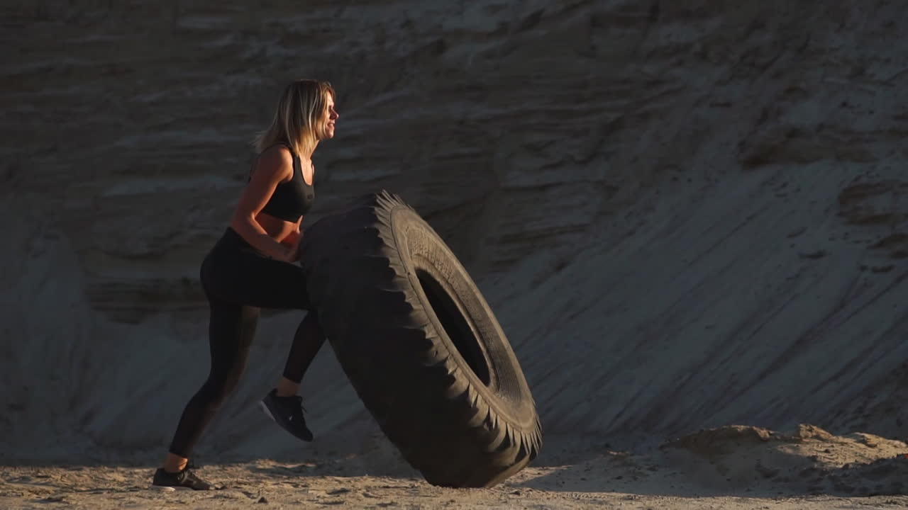 Girl in sportswear pussh a tire. Street workout.