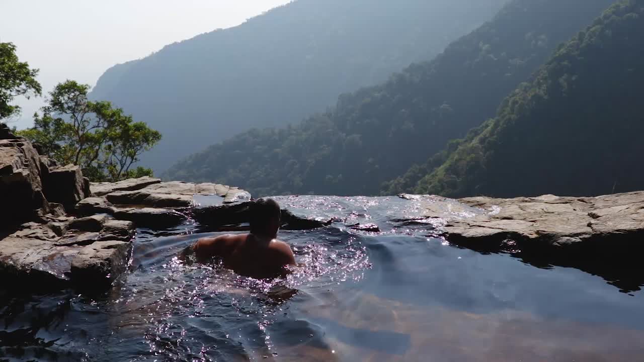 hombre nadando en una piscina natural en el acantilado de la montaña desde los ángulos superiores