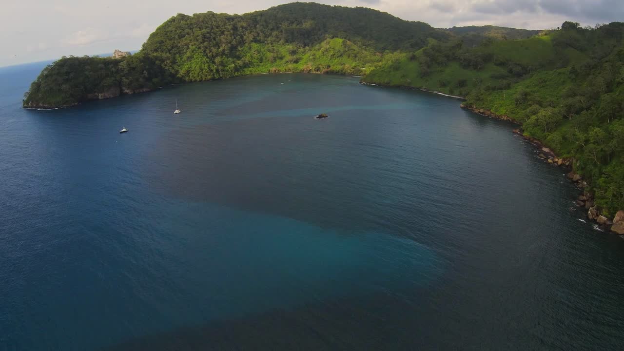 drone vuela sobre una bahía tropical con una exuberante selva y algunos barcos amarrados