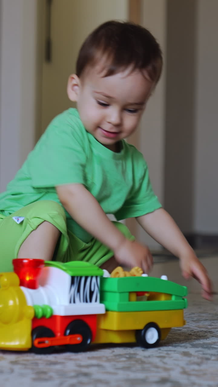 Healthy Caucasian baby boy playing with a train. Toy vehicle goes away and kid cheerfully follows it. Vertical video