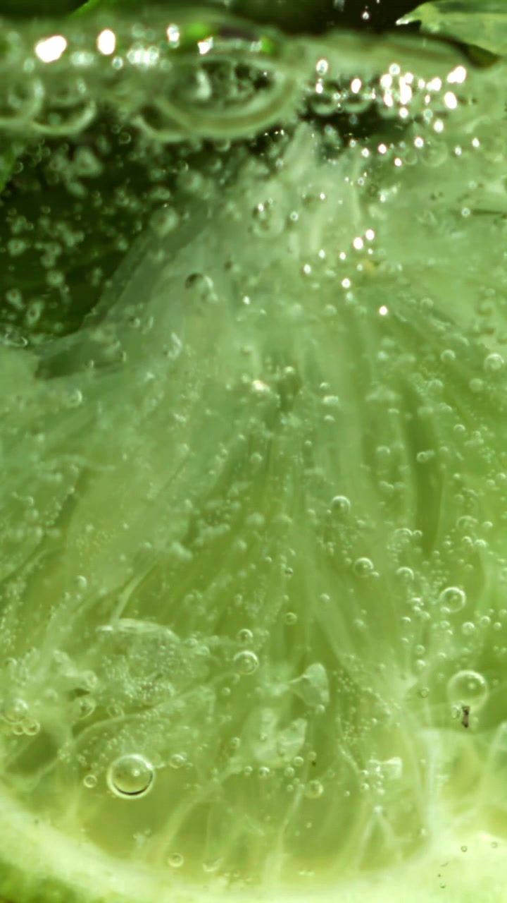 Ripresa macro di una fetta di lime fresco che effervesce in acqua gassata