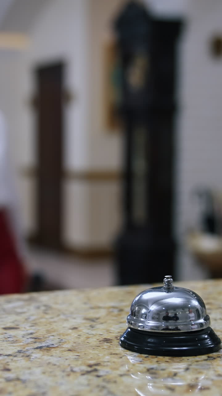 Bell button in hotel. Blurred background of woman with suitcase pressing hotel bell on table. Female client coming to a receptionist desk in vestibule for check in or check out. Tourism and travelling. Vertical video