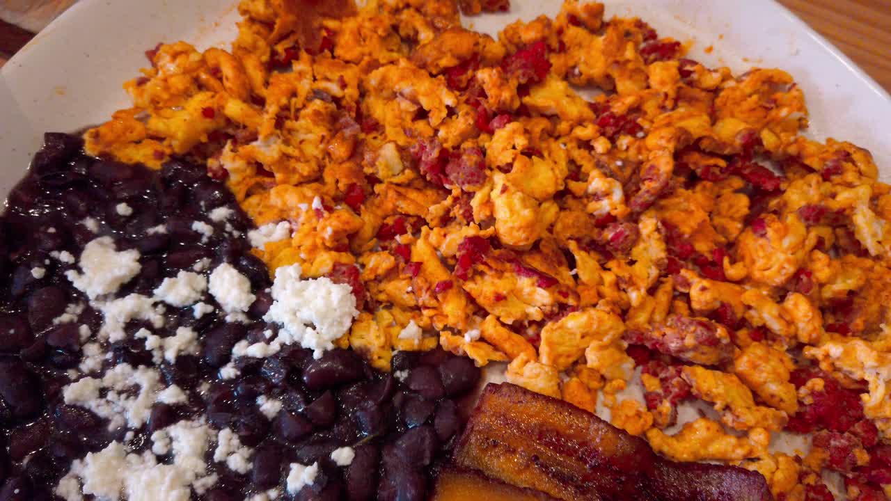 Close up of scrambled eggs mixed with chorizo, black beans topped with crumbled cheese on a white plate