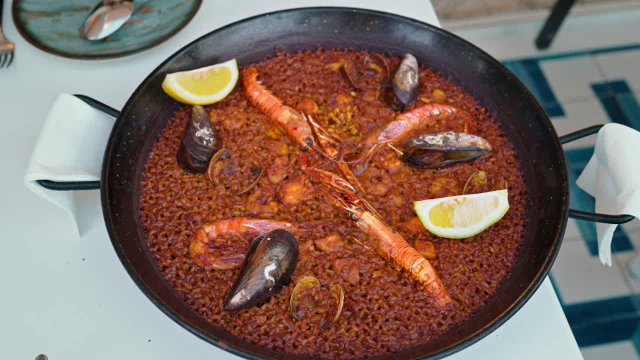 Traditional seafood paella served in a black paellera pan, garnished with lemon wedges, prawns, mussels and clams