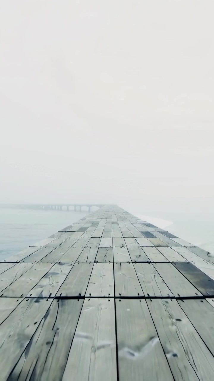 Vertikales Video: Die Kamera bewegt sich vorwärts entlang eines Holzstegs an einem nebligen See und zeigt abgenutzte Planken.