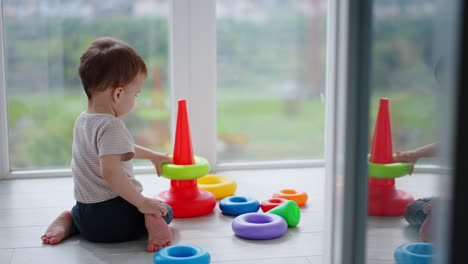 caucasian toddler sits on the floor his back to camera. lovely child playing with toy pyramid.
